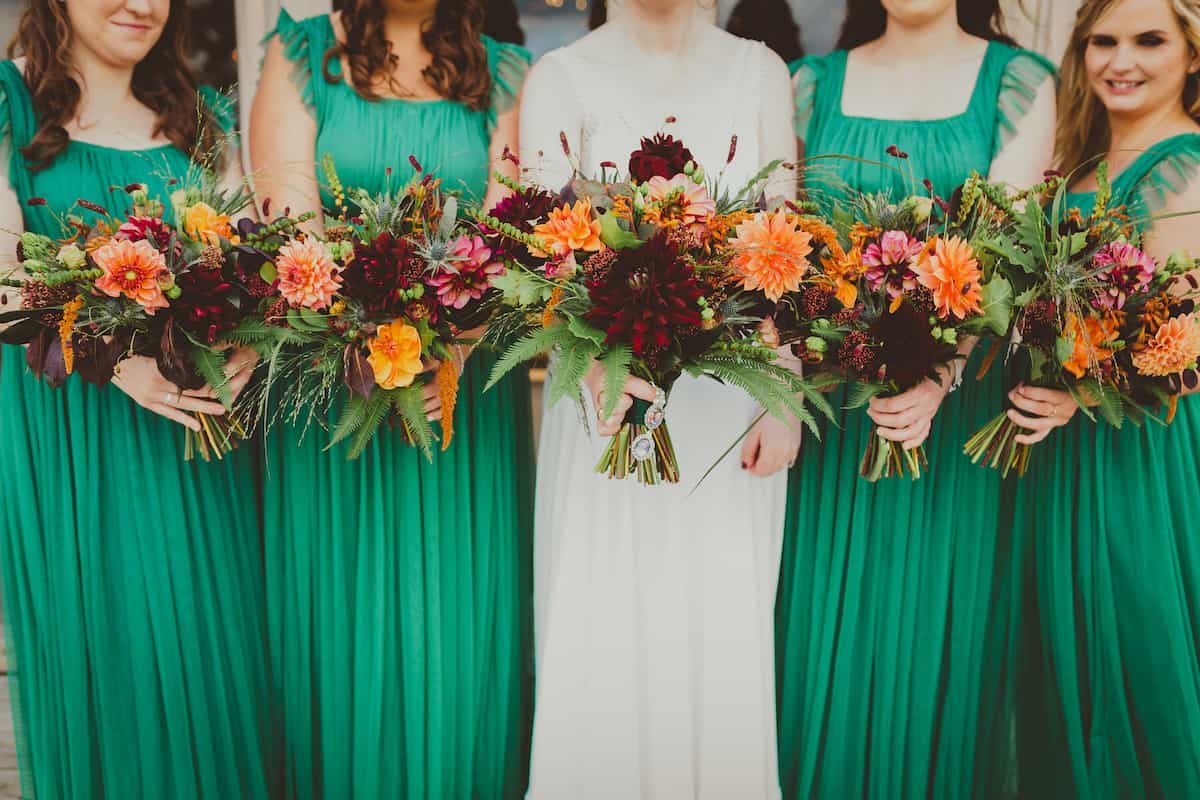 Four bridesmaids and a bride holding dark red and orange bridal bouquets