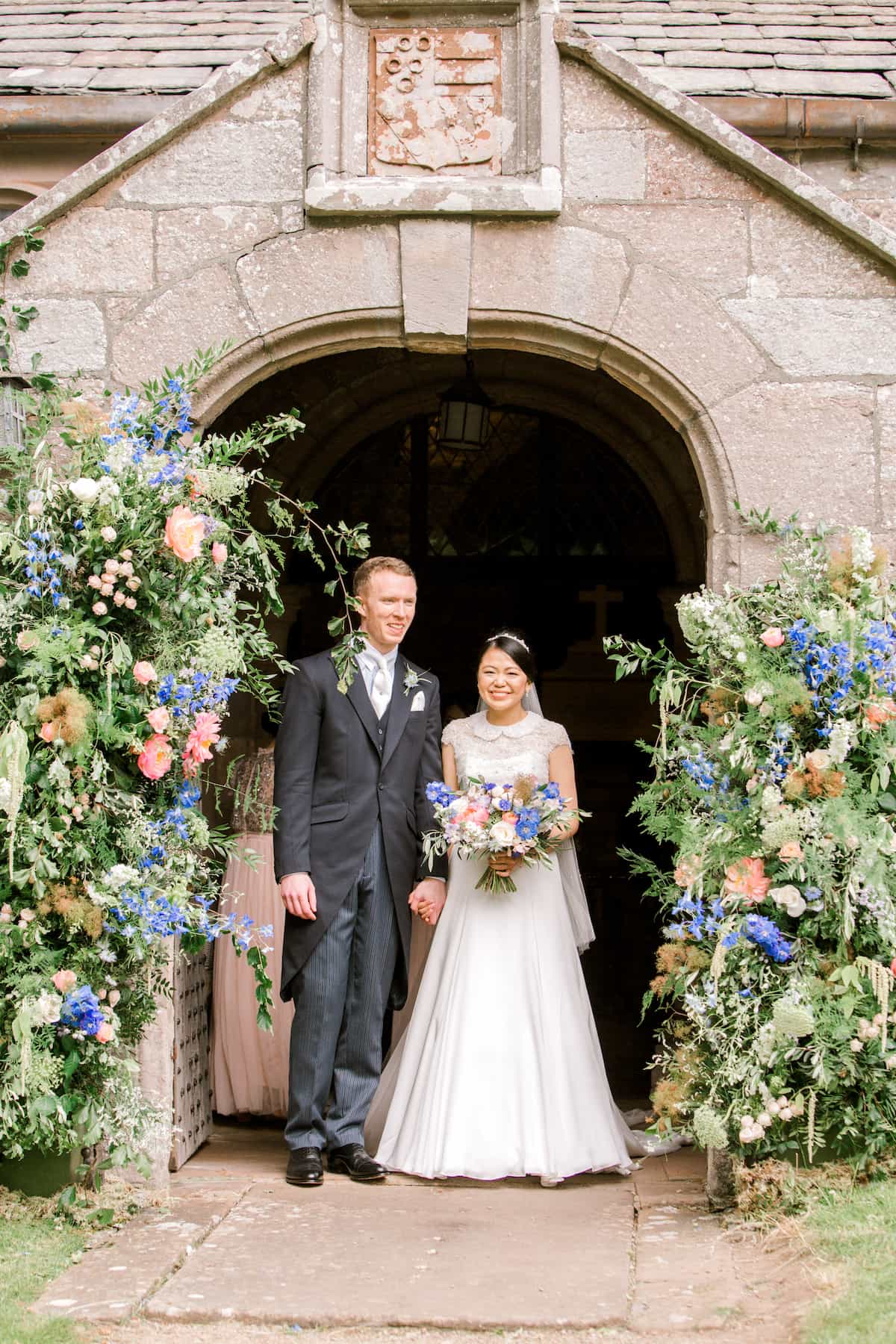 A bride and groom in a Church entrance. The bride is holding a pale blue and pink bouquet, and either side are pale blue and pink flower towers