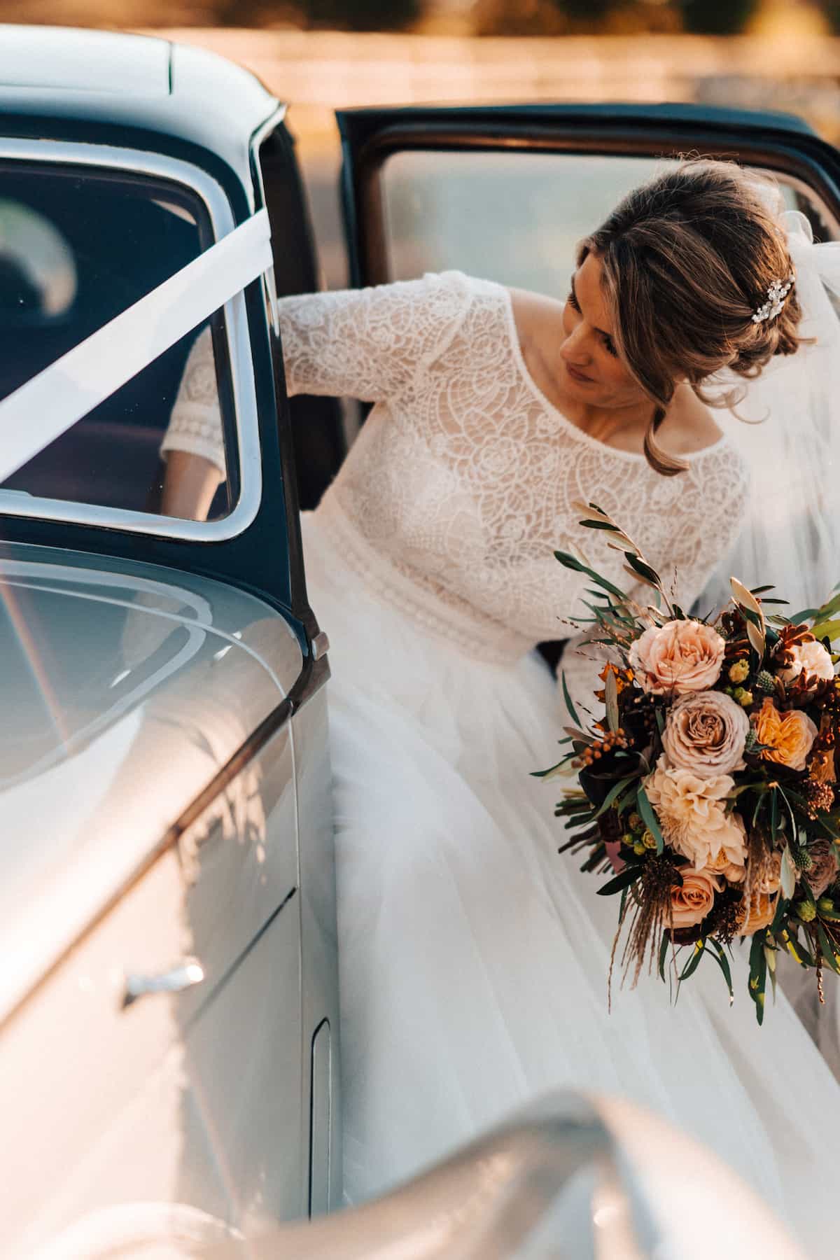 A bride getting out of a car carrying a pale pink bouquet