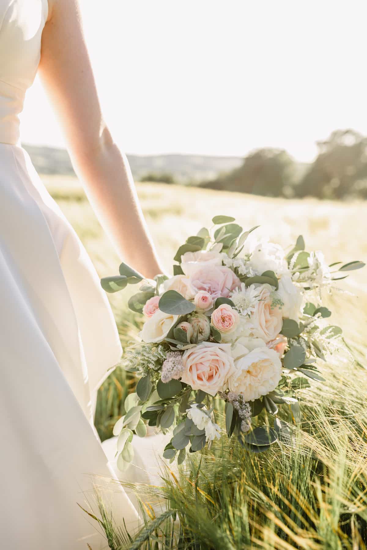 A bride holding a pale pink bouquet in a field